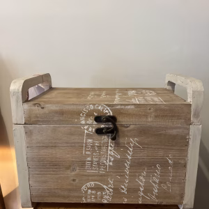 Country style wooden storage chest with a natural wood finish and decorative white word patterns on the sides, used as versatile rustic furniture