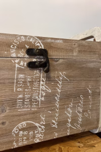 Country style wooden storage chest with a natural wood finish and decorative white word patterns on the sides, used as versatile rustic furniture