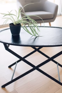 Luxury oval black leather folding table with visible perimeter stitching and black metal X-frame, styled in a modern masculine library or lounge
