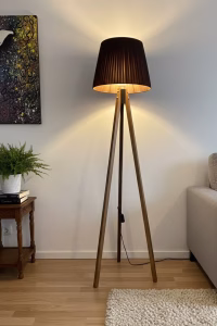 Handmade tripod floor lamp with solid walnut wood legs and a dark pleated fabric lampshade, styled in a modern living room corner