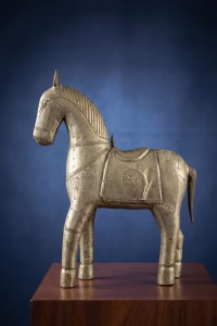 Antique hand-carved wooden horse sculpture covered in hammered copper and brass metal inlay with a rustic aged patina, displayed on a bookshelf