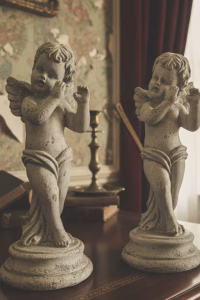 Pair of classical cherub statues with a distressed weathered stone finish, standing on circular plinths, styled on a white mantelpiece