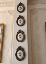 Set of four oval gold-framed wall medallions with rose-painted porcelain centers, arranged in a symmetrical vertical gallery wall layout