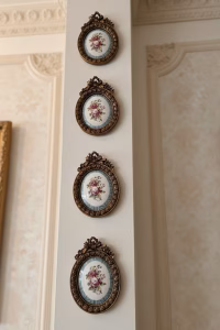 Set of four oval gold-framed wall medallions with rose-painted porcelain centers, arranged in a symmetrical vertical gallery wall layout