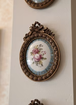 Set of four oval gold-framed wall medallions with rose-painted porcelain centers, arranged in a symmetrical vertical gallery wall layout