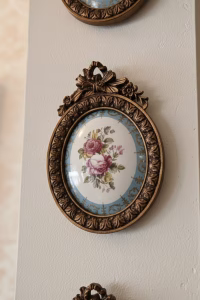 Set of four oval gold-framed wall medallions with rose-painted porcelain centers, arranged in a symmetrical vertical gallery wall layout