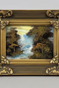 Small landscape oil-style painting in a highly detailed ornate gold Baroque frame, featuring a misty mountain stream, styled on a dark wood library shelf