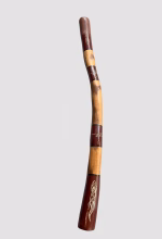 Premium master-crafted Aboriginal didgeridoo featuring bold ochre-toned bands and traditional lizard motifs set against deep earth-red panels from RockFort Lebanon
