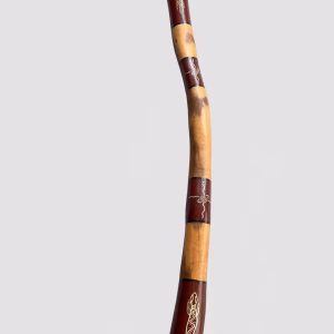 Premium master-crafted Aboriginal didgeridoo featuring bold ochre-toned bands and traditional lizard motifs set against deep earth-red panels from RockFort Lebanon
