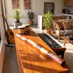 Premium master-crafted Aboriginal didgeridoo featuring bold ochre-toned bands and traditional lizard motifs set against deep earth-red panels from RockFort Lebanon