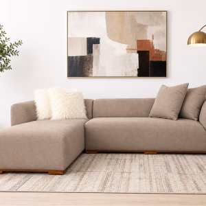 Modern beige L-shaped corner sofa with a minimalist design, deep seating cushions, and a subtle wooden base from RockFort furniture store in Lebanon.
