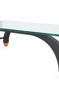 Side view of the glass coffee table showing sweeping arched charcoal grey legs and salmon orange ball feet from RockFort Lebanon.