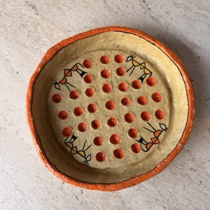 Top view of the Warli papier-mâché bowl with stick-figure folk art and a grid of raised red dots on a stone surface from RockFort Lebanon.